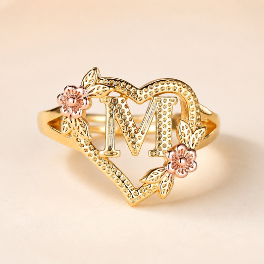 Anillo con inicial M sobre fondo rosa nude, blanco y beige