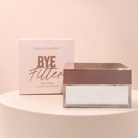 Polvo traslúcido BYE Filter de Beauty Creations sobre fondo rosa nude, blanco y beige